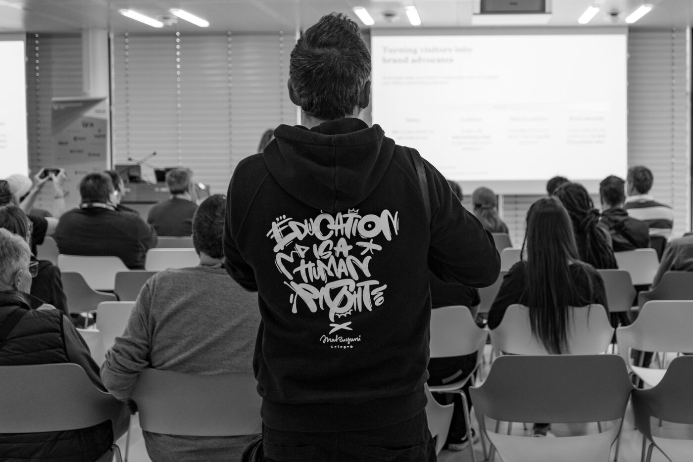 "Education is a Human Right" Text auf dem Pullover von Florian, der einen Talk beobachtet.